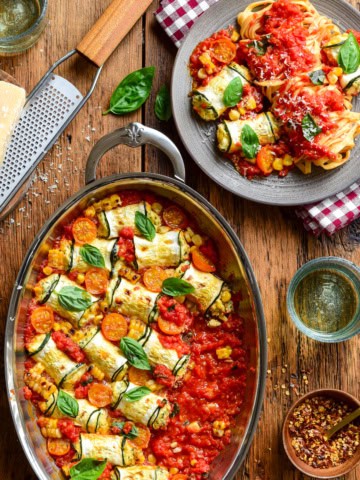 Delicious summer zucchini involtini filled with ricotta and corn, baked in a tomato sauce, garnished with fresh basil leaves, served with a side of pasta.