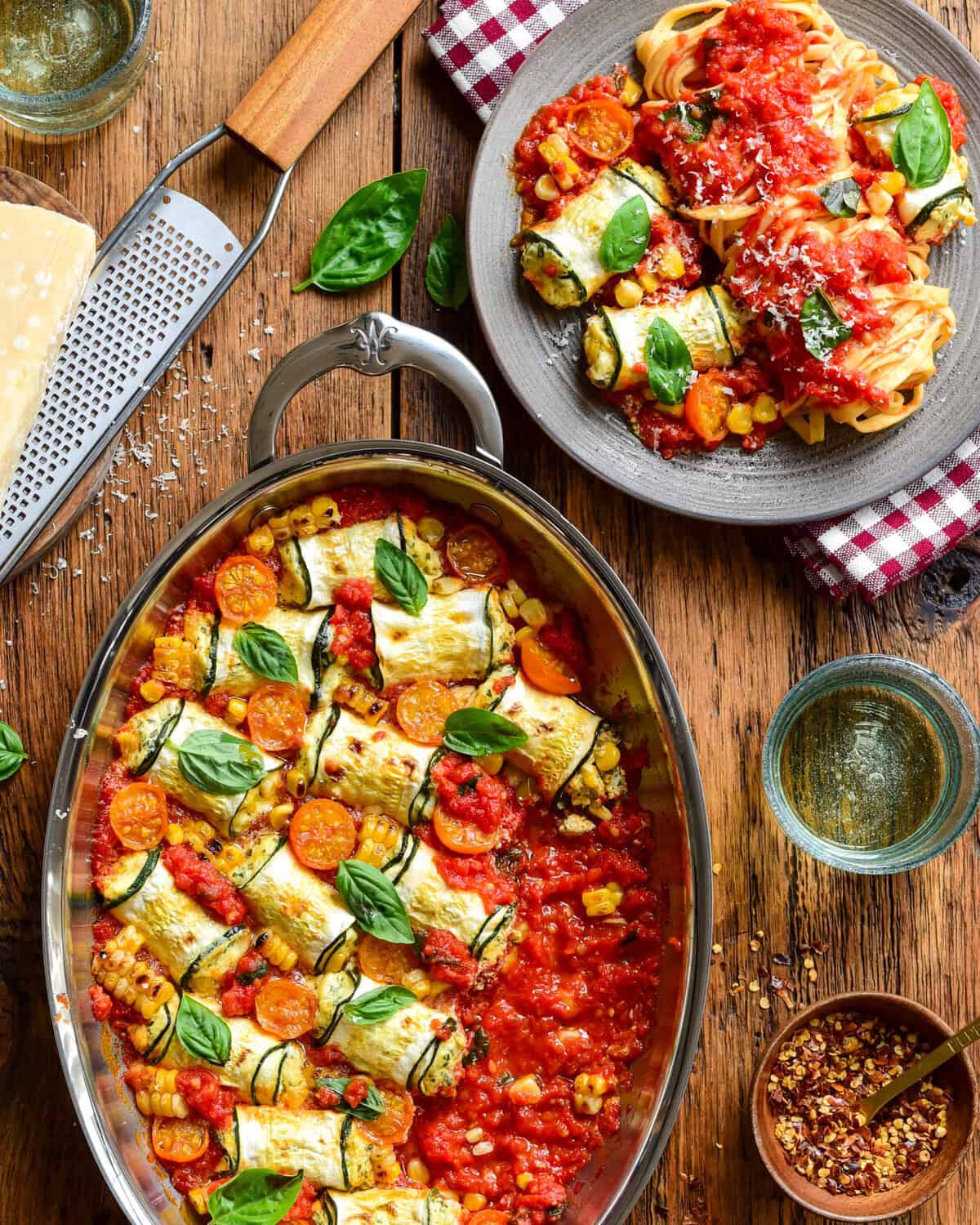 Delicious summer zucchini involtini filled with ricotta and corn, baked in a tomato sauce, garnished with fresh basil leaves, served with a side of pasta.