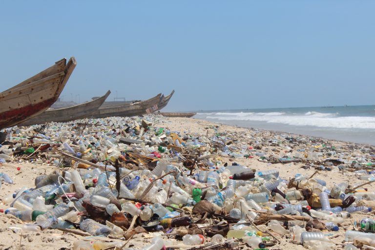 Plastic waste pollution on Ghana’s beach with abandoned boats in the background.