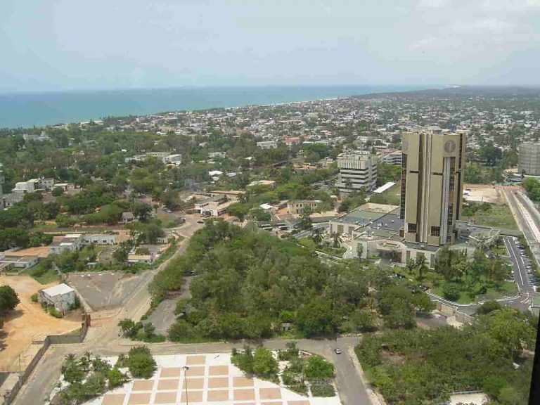 Aerial view of Lomé, Togo, showing city buildings, greenery, and the Atlantic Ocean in the backgroun.