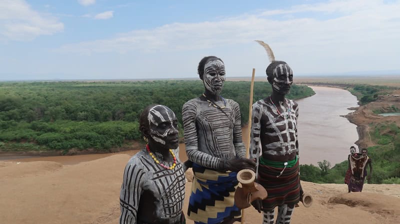 African tribes with body paint and traditional attire near a river.