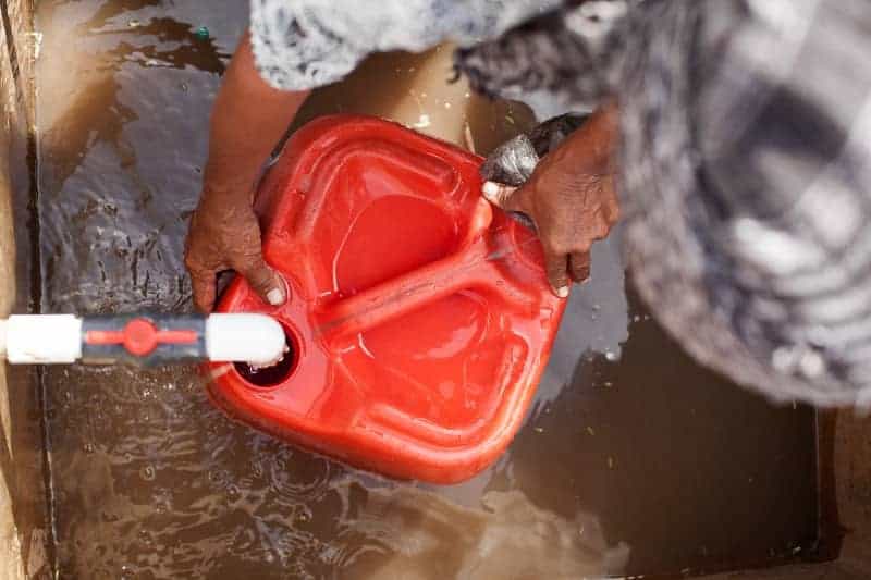 Person filling a red water container with clean water in Africa.
