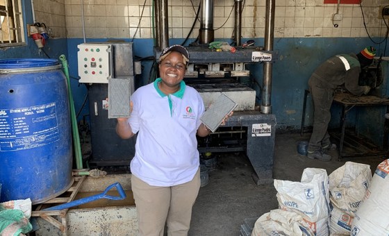 Woman smiling in workshop with machinery and supplies, promoting climate solutions in Africa.