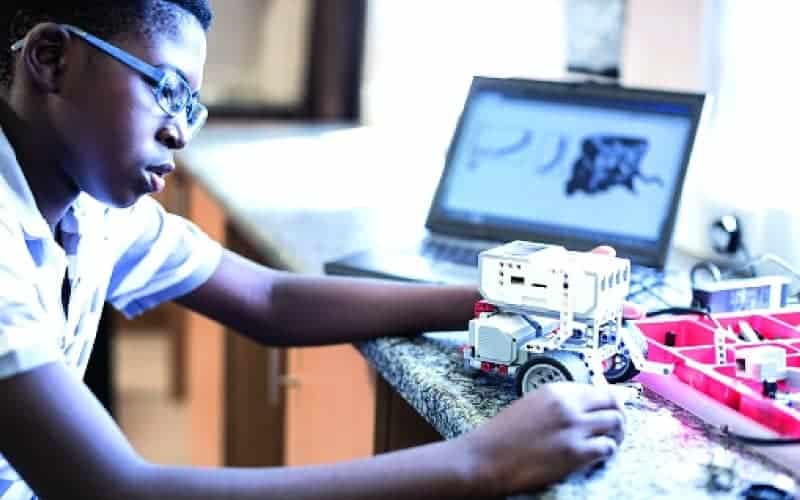 Young African girl working on robotics with a laptop and AI tools.