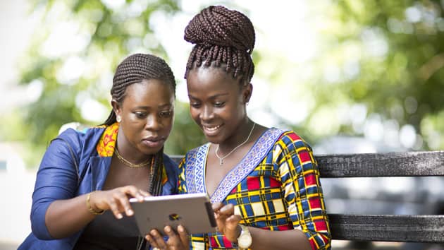 Two African women entrepreneurs using a tablet outdoors.