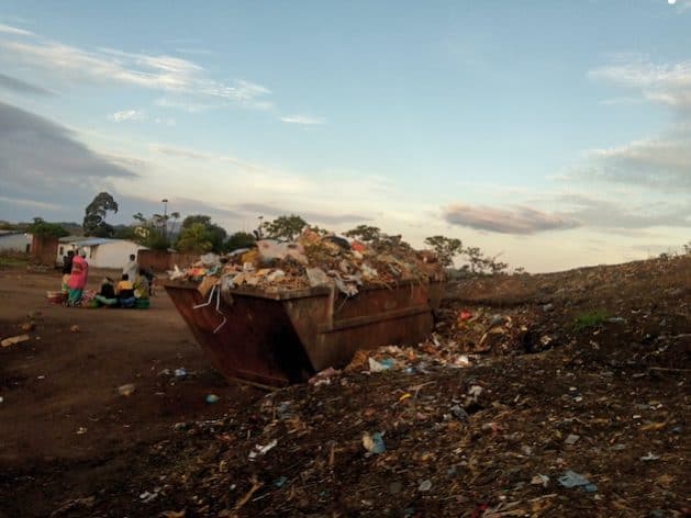 Open trash dump with scattered waste and debris in a rural area.