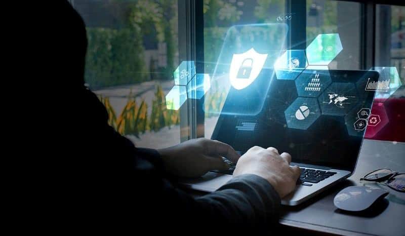 Person working on a laptop with cybersecurity icons and digital security graphics.