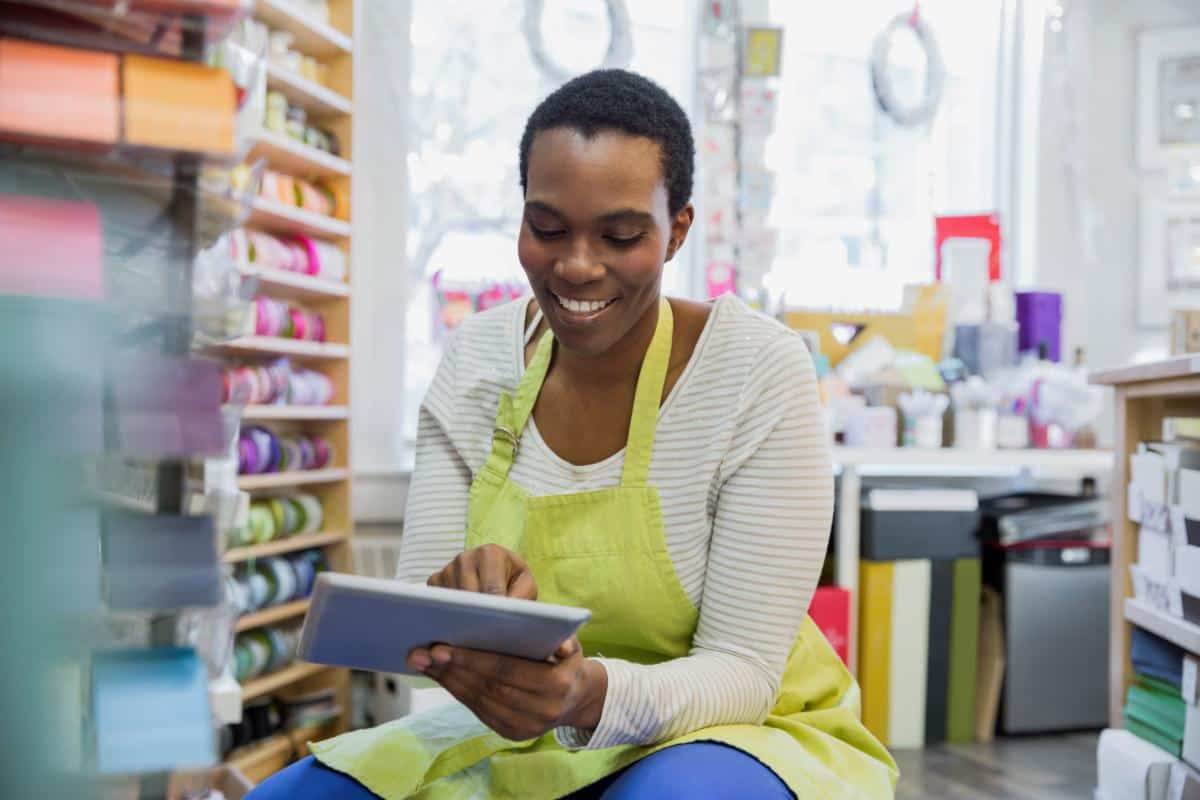 Woman using a tablet in a retail store with shelves of products in the background.