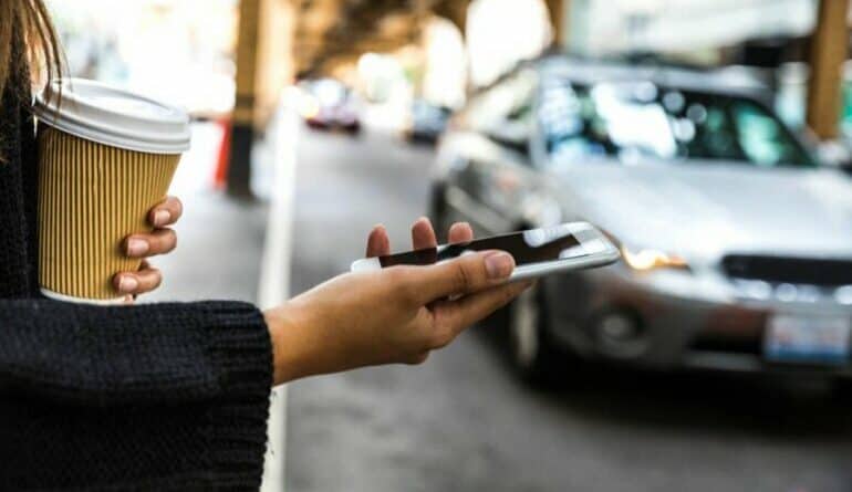 Young person using smartphone on city street with cars in background.