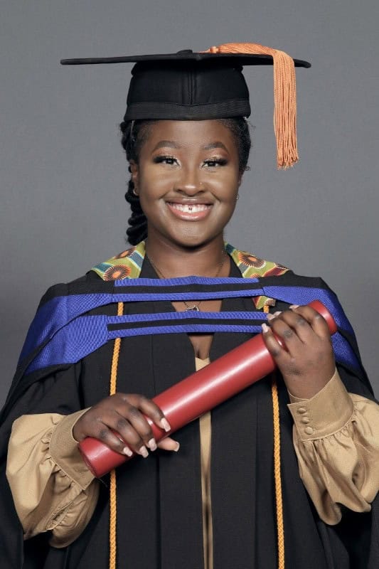 Young female graduate in cap and gown holding diploma, breaking barriers in cybersecurity.
