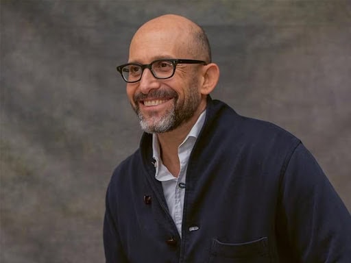 Man smiling, wearing glasses, in a professional setting, promoting health initiatives.