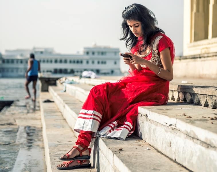 Woman using smartphone on riverbank, highlighting digital access and gender digital divide issues.