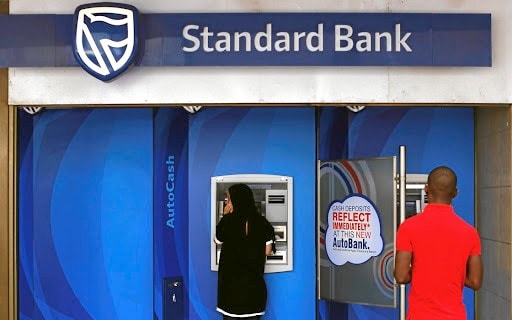 Customers using Standard Bank ATM for banking transactions outdoors.