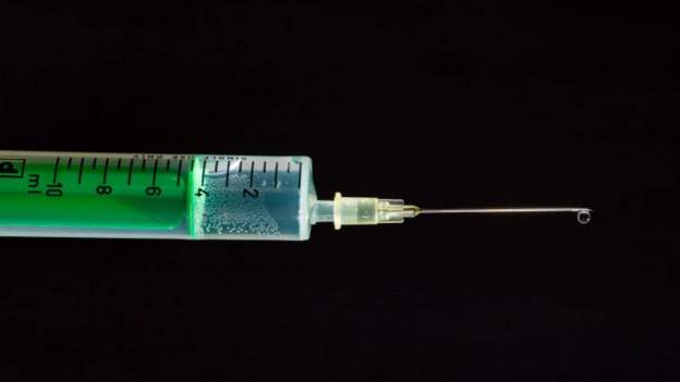 Close-up of a vaccine syringe with a needle on a black background.