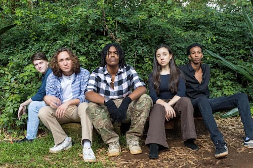 Young musicians sitting outdoors in a forest setting.