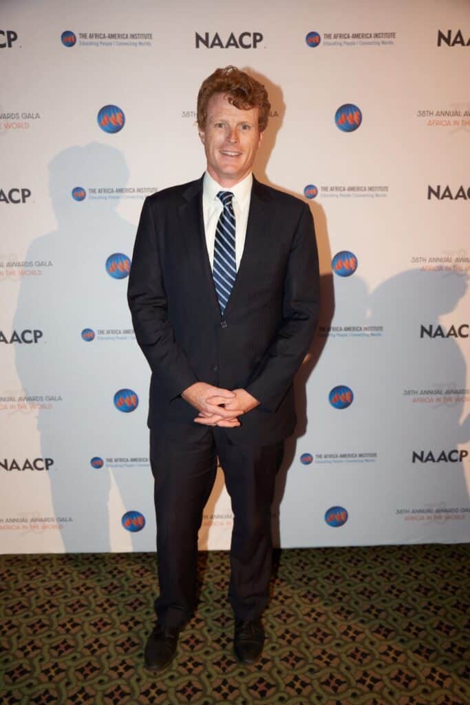 A man in a suit standing at the NAACP event with a backdrop featuring the NAACP logo and "Africa in.