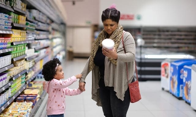 Woman and child shopping with clear food warning labels in a supermarket aisle.