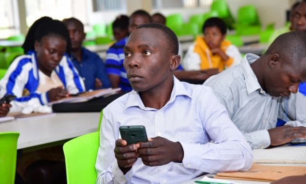 Ugandan students using mobile devices for digital learning during COVID-19.