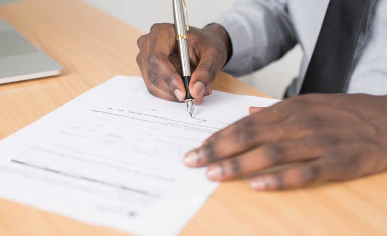 Close-up of a person signing an official document on a wooden desk.