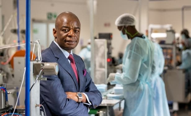 Business leader in African manufacturing plant with healthcare workers in background.