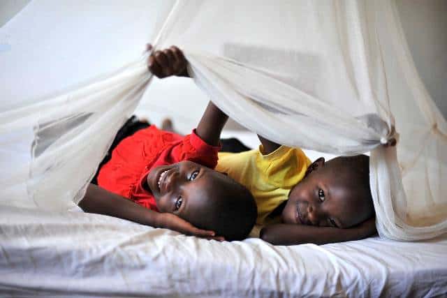 Two children lying under a mosquito net, highlighting malaria prevention efforts in Africa.