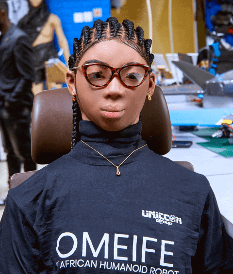 Young woman with braided hair and glasses at tech event showcasing Omeife robot.