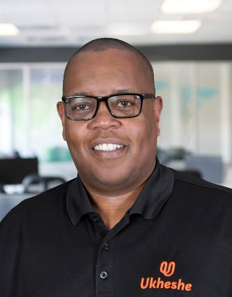 Man smiling in office wearing Ukheshe branded shirt, representing African financial innovation.