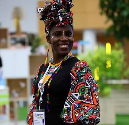 Colorful African woman wearing traditional dress and headwrap at WTM Africa event.