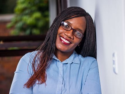 African woman smiling, wearing glasses, and celebrating International Women’s Day.