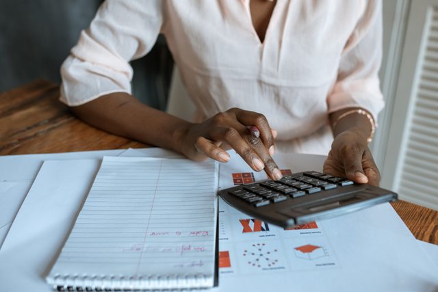 Woman calculating business startup funds with calculator and notes.