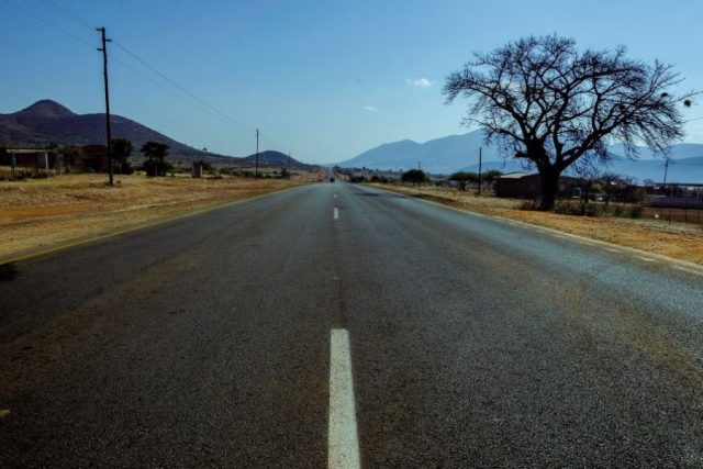 Road in rural landscape with mountains and trees under clear sky.