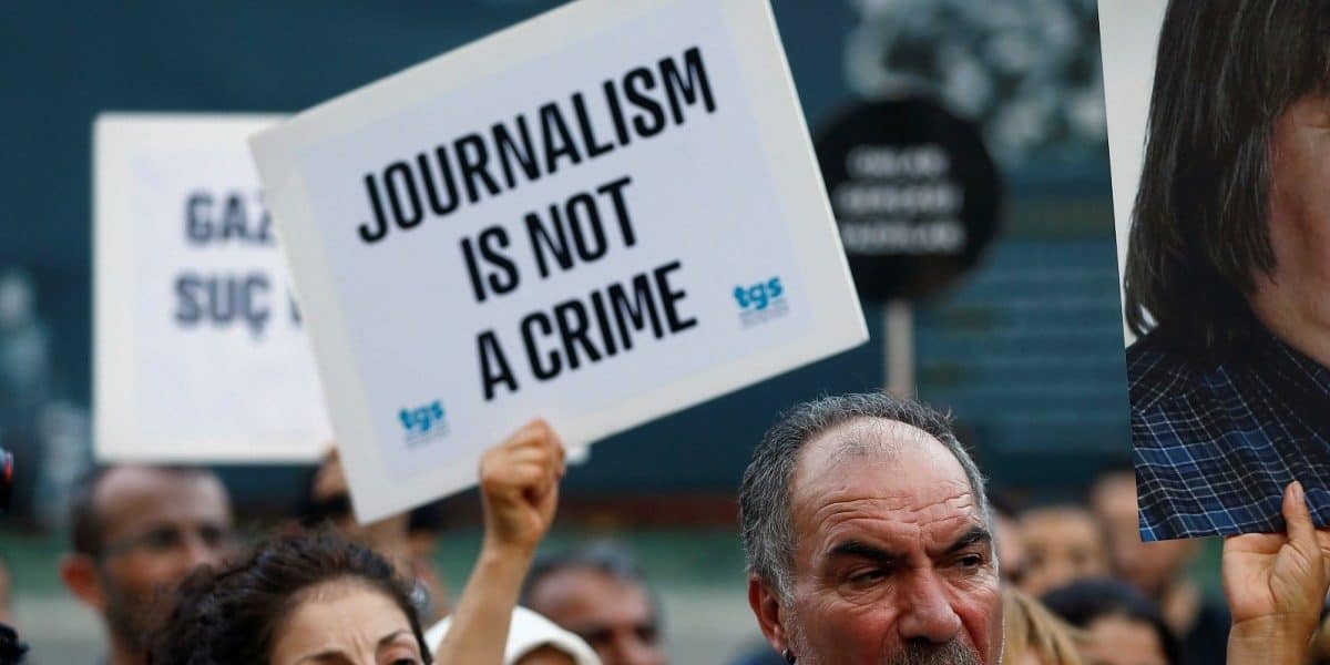 Protesters hold signs advocating for press freedom and emphasizing that journalism is not a crime.