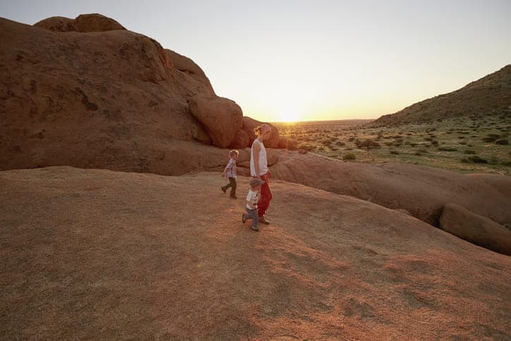 Family exploring Namibia desert at sunset with rocky formations in the background.