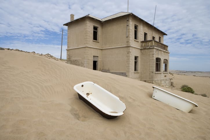 Old house surrounded by sand dunes in Namibia's desert landscape.