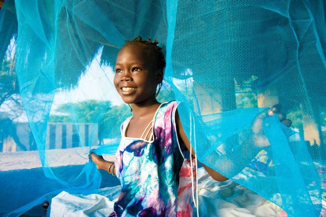 Child smiling inside a malaria prevention tent in Africa, symbolizing hope and health progress.