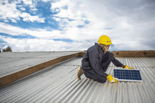 Solar panel installation worker on a rooftop in Kenya with a solar panel.