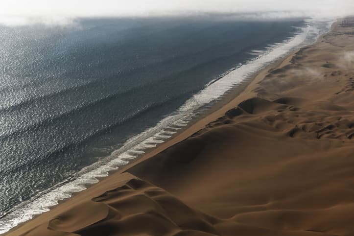 Sand dunes and ocean coastline in Namibia at sunset.