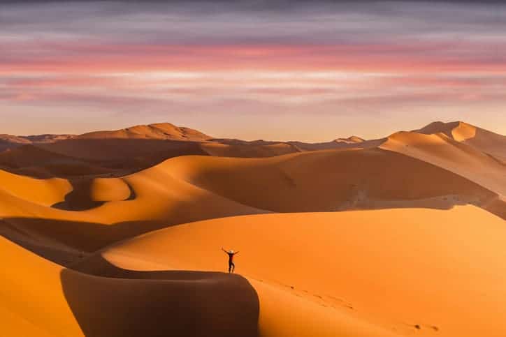 Desert dunes at sunset in Namibia, showcasing vast sand landscapes and vibrant sky colors.