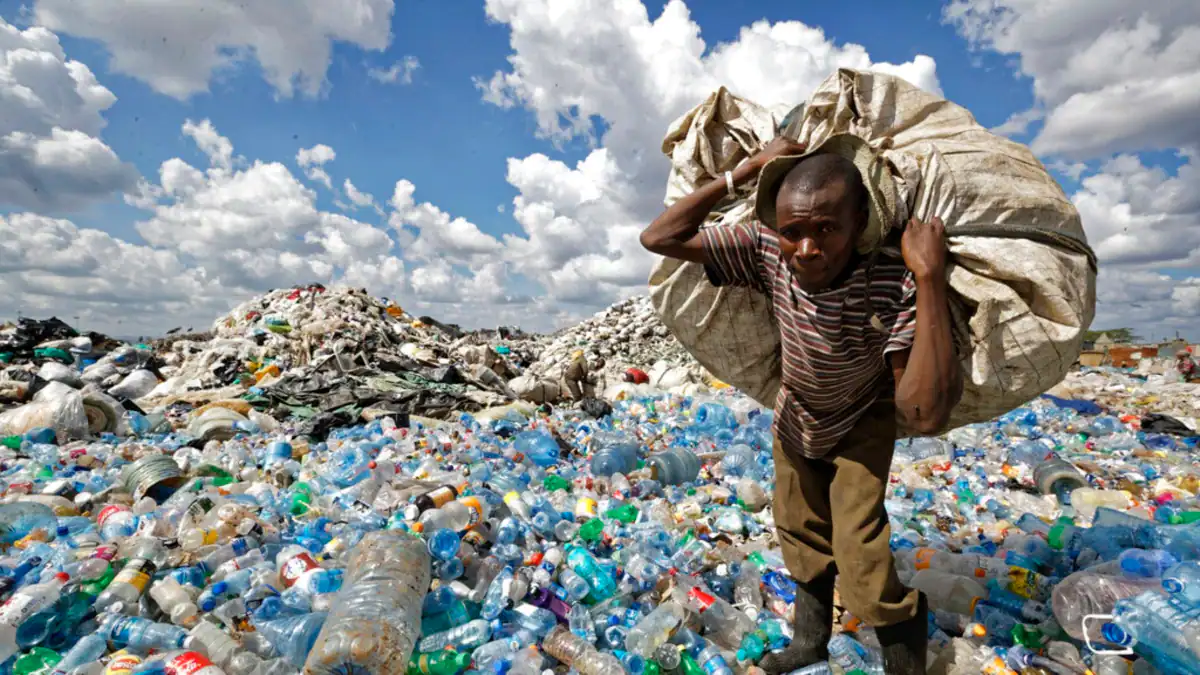 Child carrying a large bag of plastic waste amid heaps of bottles.