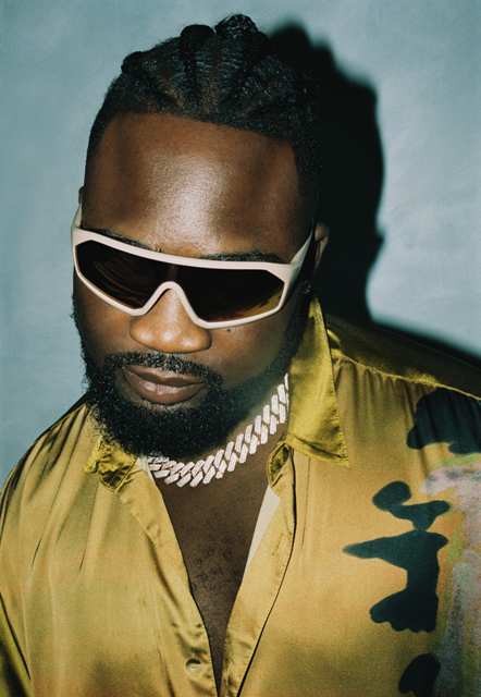 Blaq Jerzee wearing sunglasses and a yellow camouflage shirt, showcasing his unique style in the Afr.