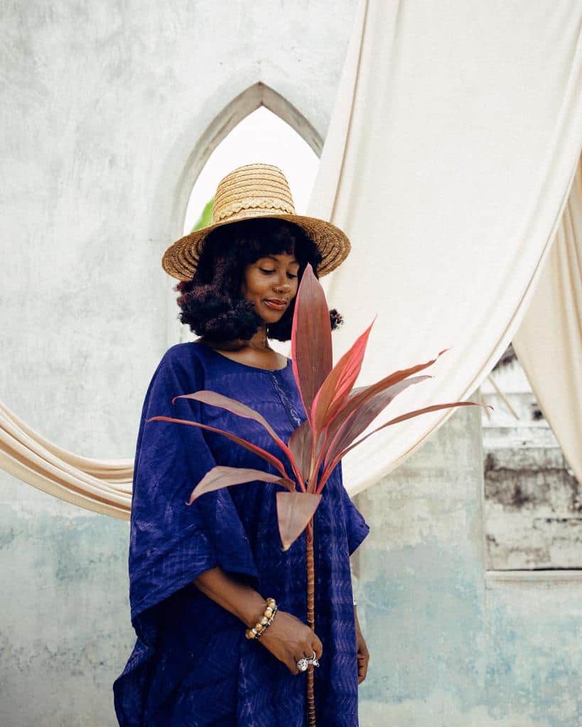 Woman in blue dress with hat holding a plant at Ghana wellness studio launch.