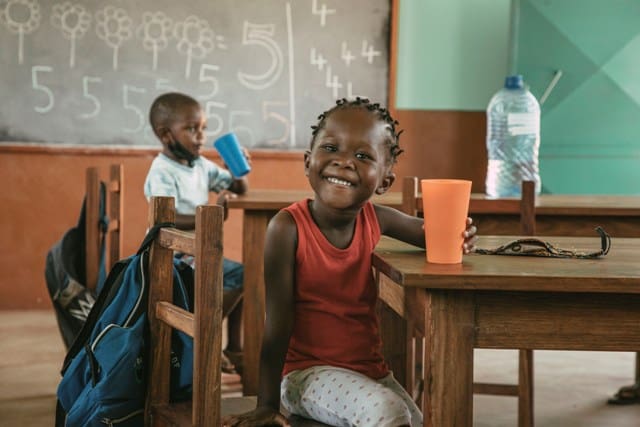 Children in classroom smiling, with school supplies and water bottle.