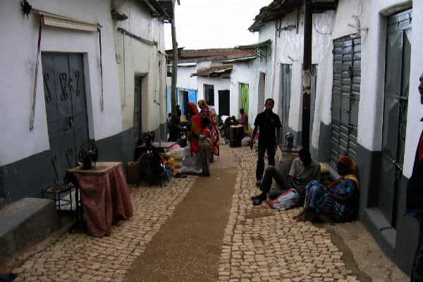 People gather in a narrow street of an African neighborhood with colorful houses.