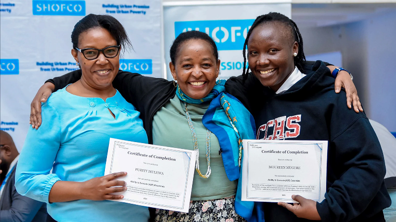 Women in Kenya celebrating success with certificates at SHOFCO program.