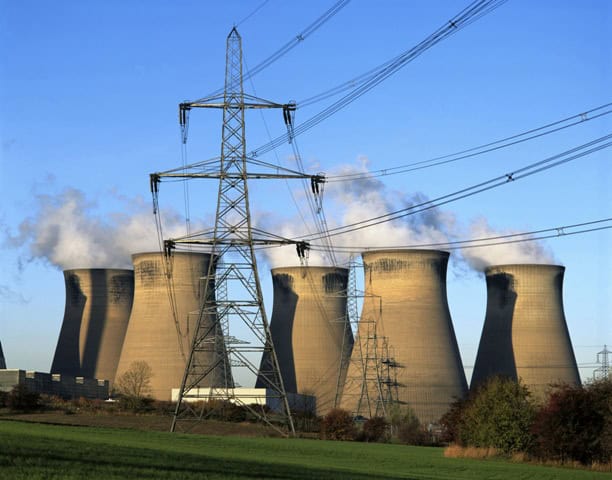 Nuclear power plant cooling towers with power lines against blue sky.