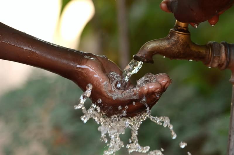 Hand turning on water tap, emphasizing water resource management and conservation.