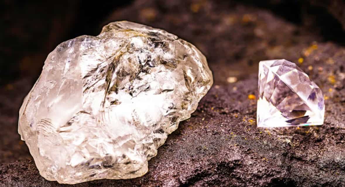 Diamond mineral and cut gemstone on dark soil surface.