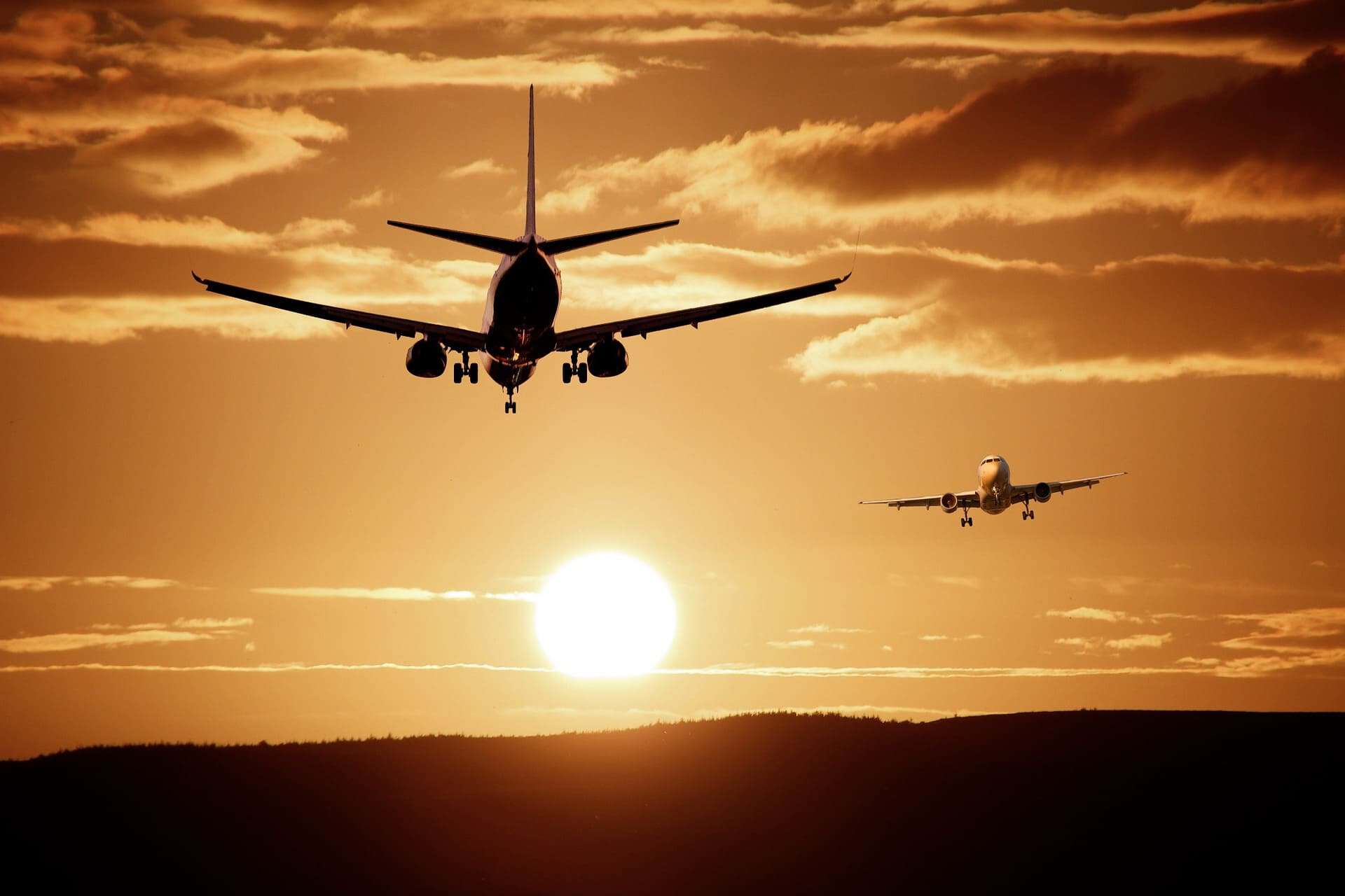Two airplanes landing at sunset with a vibrant sky and horizon.