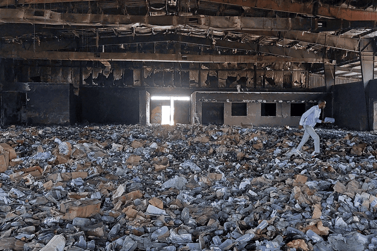 Fire-damaged building with rubble and a person walking through the destruction in Sudan.