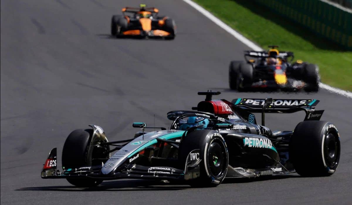 Formula 1 cars racing on a track in Kigali, Rwanda, with lush green surroundings.